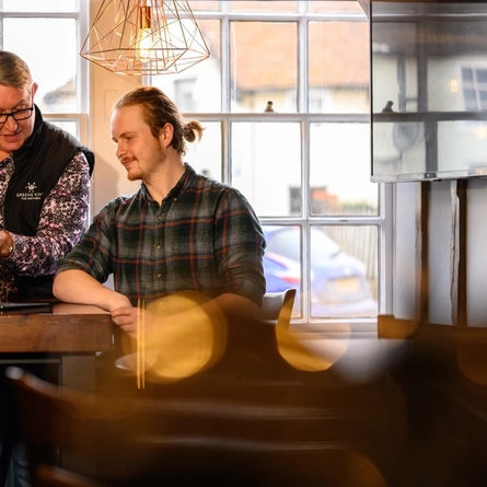 two men sat at a table looking at a laptop