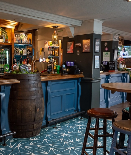 The blue, wood panelled bar inside The Royal Oak in Bishops Cleeve, with a large beer barrel built into the counter.