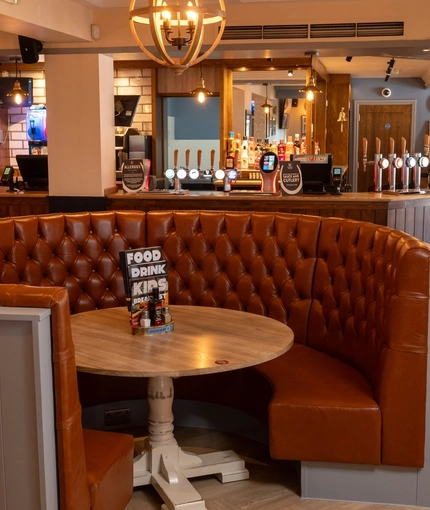 The bar and interior seating area at The Weathervane, with a circular booth seat around a round wooden table.