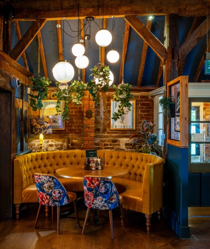 An interior circular booth seating area at The White Hart, with wooden beams, upholstered seats, and potted plants hanging above the table.