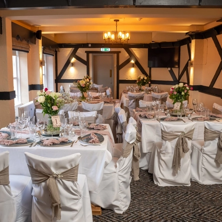 The function room at The Cherry Tree, set up for a wedding; with a TV on the wall, white tablecloths and seat covers, pink napkins, and vases of flowers on each table.