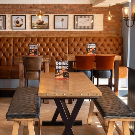 An interior restaurant seating area at The Weathervane, with upholstered chairs, benches, and booth seats, and framed artwork on the wall.