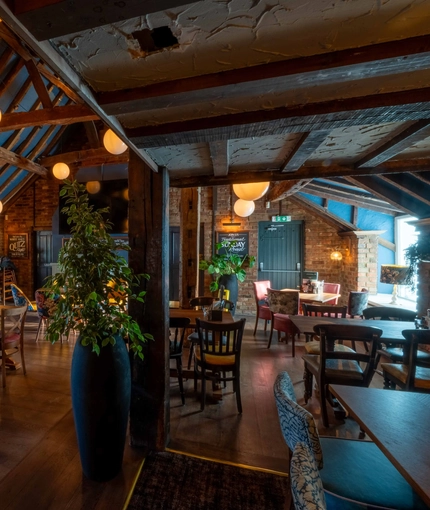 The interior restaurant seating area of The White Hart, with wooden beams, and a TV on the wall.