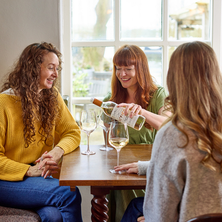 An image of 3 people sat around a table within the interior seating area enjoying glasses of white wine at a Chef & Brewer venue.