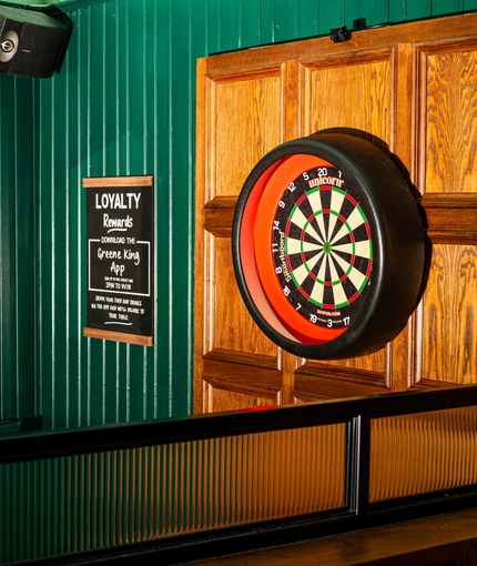 A close up view of a dartboard and framed artwork on a wall inside the Lord Raglan.