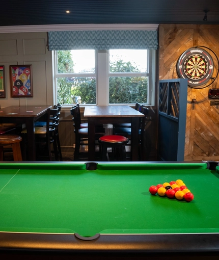 An interior seating and games area at The Horsforth, with a pool table, a TV on the wall, and a dartboard.
