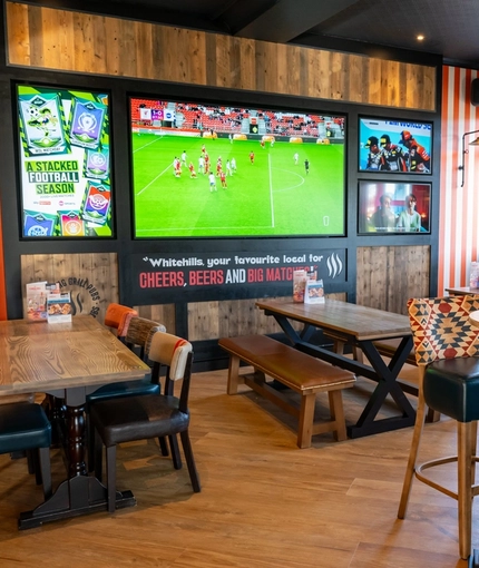 The interior restaurant seating area at Whitehills in Northampton, with TVs on the wall, and upholstered seats.