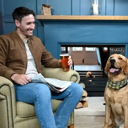 A man drinking a pint in the pub with his dog sat next to him