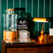 A close up view of the self-serve water station inside The Junction, with a glass water dispenser and upturned highball glasses standing on golden drinks trays, on a wooden cabinet.