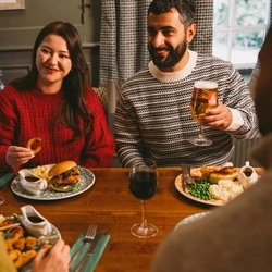 A group of people seated at a festive decorated table near a Christmas three. There are plates of food and drinks in front of them.