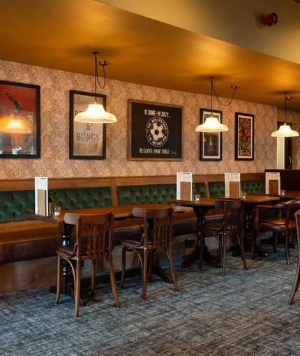 An interior restaurant seating area at The Richmond Arms, with a long upholstered booth seat along one side of the room; and framed artwork on the walls.