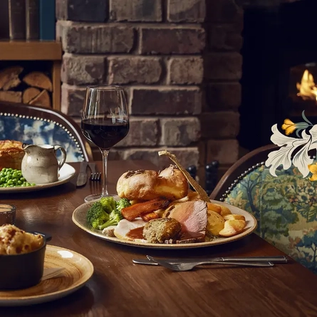 A roast dinner on a table next to a glass of red wine.