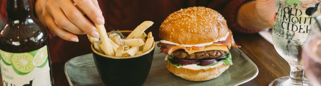 Bacon cheeseburger in a sesame-seed bun with lettuce, red onion and mayonnaise, served with rosemary-topped chips and Old Mout cider.
