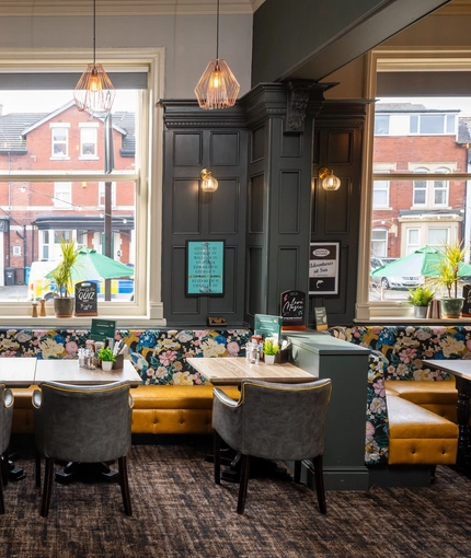 An interior restaurant seating area at The Victoria, with an upholstered corner seat beneath the window, wood panelled walls, a fireplace, and a TV on the wall above it.