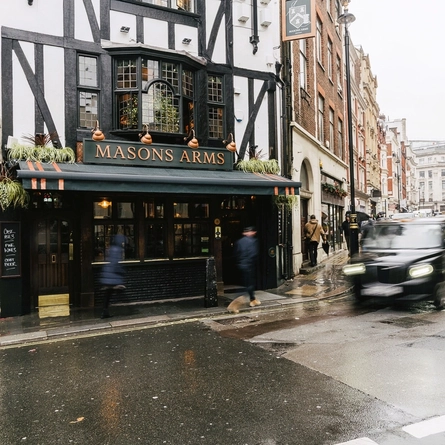 The exterior facade and signage of the Masons Arms in Mayfair, with a view of the rest of the street.