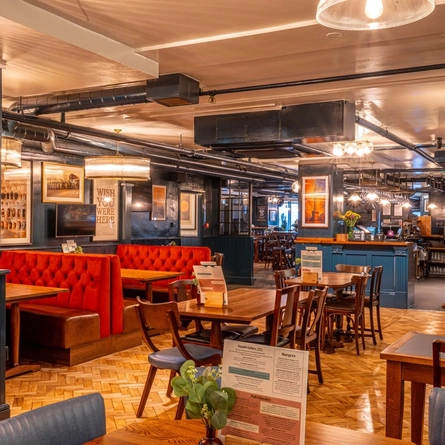 The interior restaurant seating area at the Monument, with wooden tables and chairs, booth seating, and a TV on the wall.