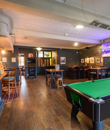 Interior dining area of a pub with a TV and a pool table.