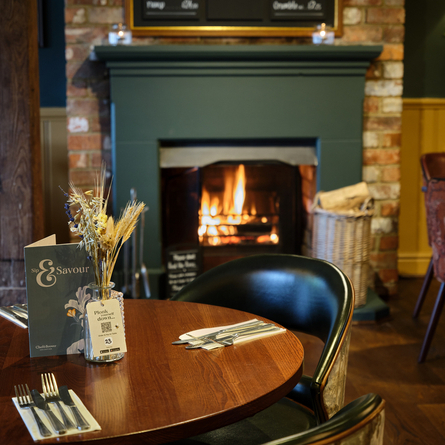 The interior restaurant seating area with wooden tables, upholstered seats, wooden beams, and fireplace, at the Smiths Arms pub in Beckwithshaw.
