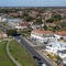 Aerial coastal view of Bournemouth with a wide sandy beach beside blue sea, grassy cliff-top gardens with winding paths, and rows of houses and apartments including The Commodore along the seafront road.