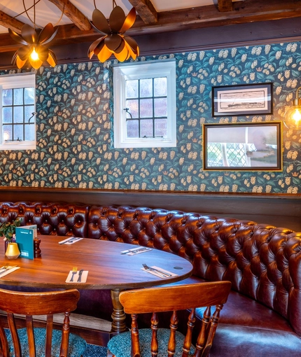 An interior restaurant seating area at The Walkford, with a curved, upholstered booth seat, a large oval wooden table, and framed artwork on the walls.