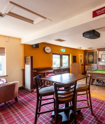 Interior dining area of a pub with a bar, a dartboard, a TV and a pool table.