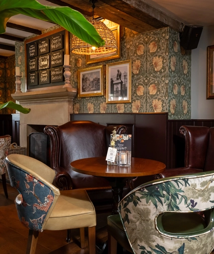 An interior restaurant seating area of The Hollybush, with upholstered chairs, wooden beams, and a fireplace.