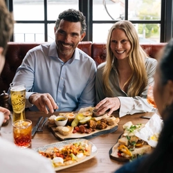 A mixed group of people seated at a wooden table enjoying plated sharing dishes.