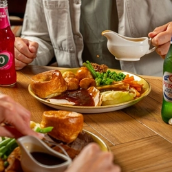 An image of gravy being poured over a Sunday Roast with various drinks within the interior restaurant and seating area at a Hungry Horse venue.
