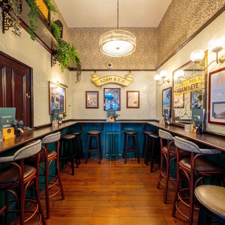 An interior restaurant seating area at Adam & Eve, with plants sitting on a shelf, and framed artwork on the walls.