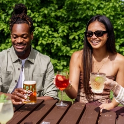 A mixed group of people, sitting at an outdoor table, enjoying a variety of drinks and conversation.
