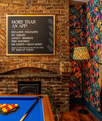 The interior games area at The Windmill Inn, with a pool table, a TV on the wall, and a large brick fireplace.