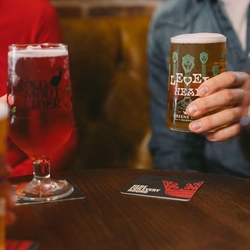 People at a pub table holding drinks, including a pint of Level Head beer and a glass of red Old Mout cider, with other drinks in the foreground.