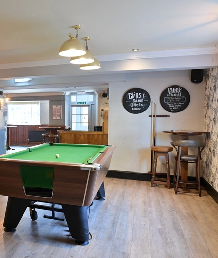 Interior seating area of a pub with a bar, a pool table and a gambling machine.