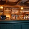A close up view of the bar inside The Rising Sun in Wistaston, with stone flooring, wooden beams on the ceiling, and wine glasses hanging in racks above the counter.