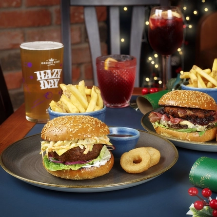 An advertising image of 2 plated Burger dishes and a selection of drinks sat on an interior table within the restaurant and seating area at an Urban Core venue.