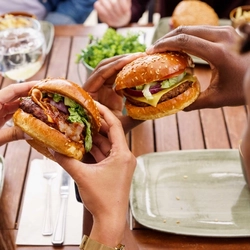 An exterior shot of people enjoying drinks and burgers within the beer garden seating area at a Community Pub with Food venue.