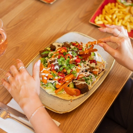 A lifestyle image of people enjoying a plated Lamb Kofta Flatbread at an indoor table.