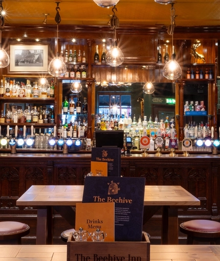 The bar and interior restaurant seating area at The Beehive Inn, with a TV hanging from the ceiling, bar stool seating, and gothic window style carvings on the front of the bar.