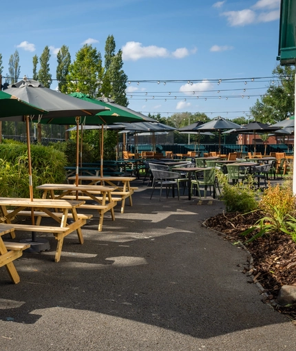 The exterior beer garden seating area at the Rudds Arms; with wooden picnic tables, shade umbrellas, and string lights overhead.
