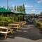 The exterior beer garden seating area at the Rudds Arms; with wooden picnic tables, shade umbrellas, and string lights overhead.