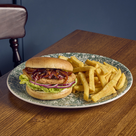 A vegan burger and fries served on a plate which sits on a wooden restaurant table.