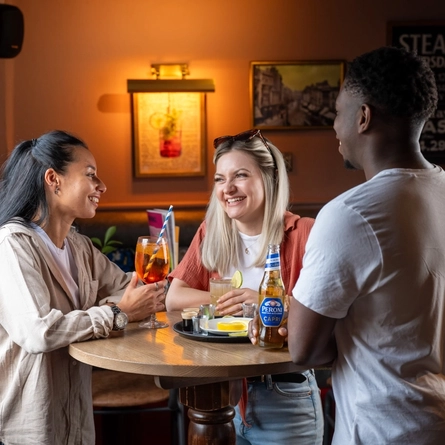 3 friends stood round a table with drinks and shots 