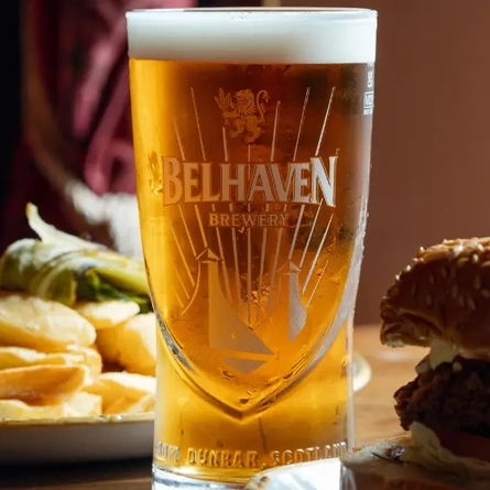 An advertising image of a pint of Belhaven Belter sat within an interior restaurant seating area.