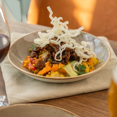 A bowl of Crispy Duck Salad which sits on a cloth napkin on a wooden table, between a glass of red wine and a glass of beer.