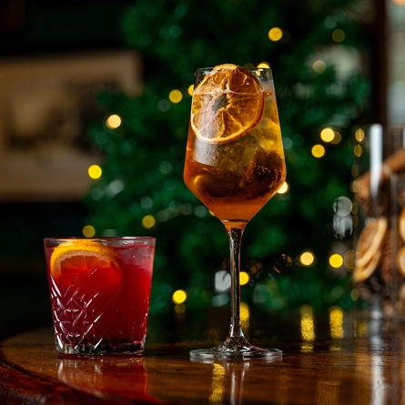 Two cocktail type drinks on a bar.  One in a low ball tumbler and the other is in a stemmed glass.