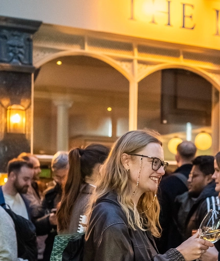 An image focusing on 2 friends enjoying glasses of white wine and celebrating with a cheers stood outside The Kings Stores.