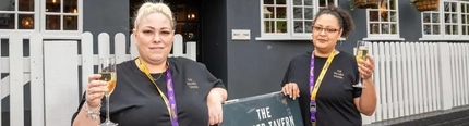 Two women holding glasses of champagne outside of a pub.