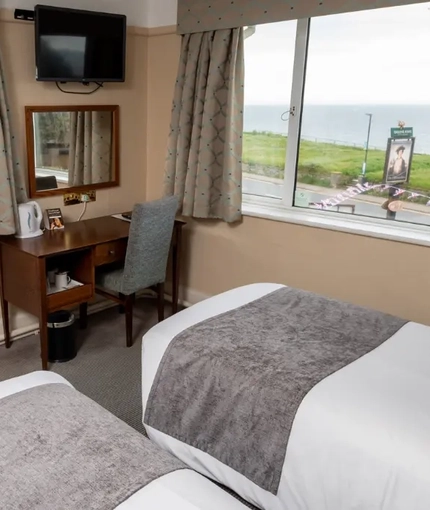 A interior twin hotel bedroom with two single beds, a dressing table with mirror and TV at The Commodore.