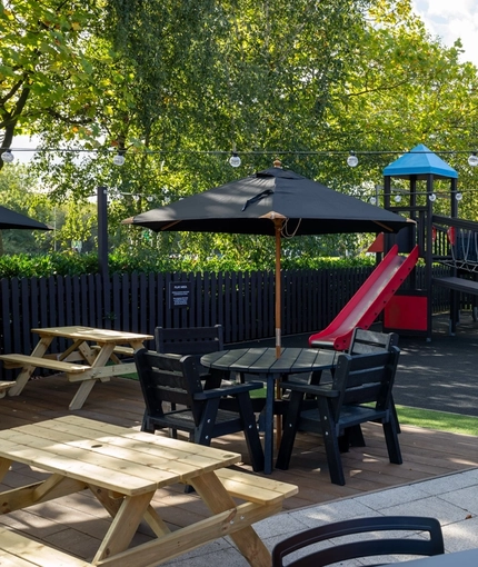 The exterior beer garden seating area with tables, chairs, wooden bench seating, children's play area and string lighting at The Castle View.