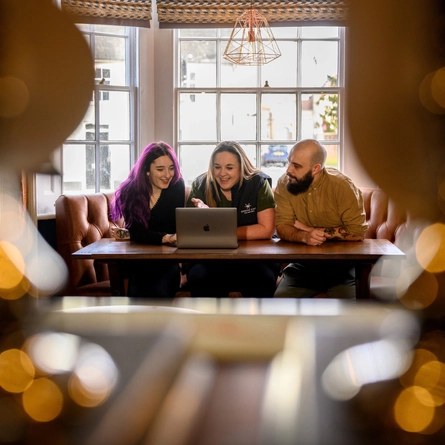 Two Women and a Man sat at a table looking at a laptop in front of them